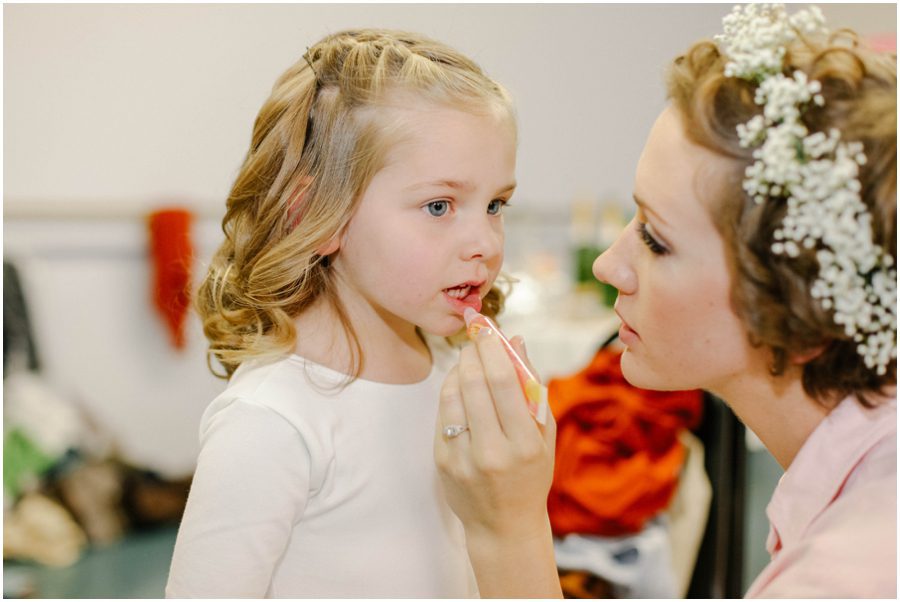 photo of a bride putting makeup on flower girl