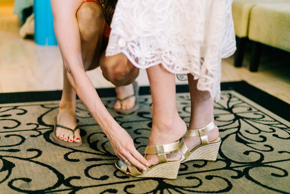 Photo of the maid of honor helping the bride put on her wedding shoes. Destination wedding at the Postcard Inn on the Beach by Catherine Ann Photography