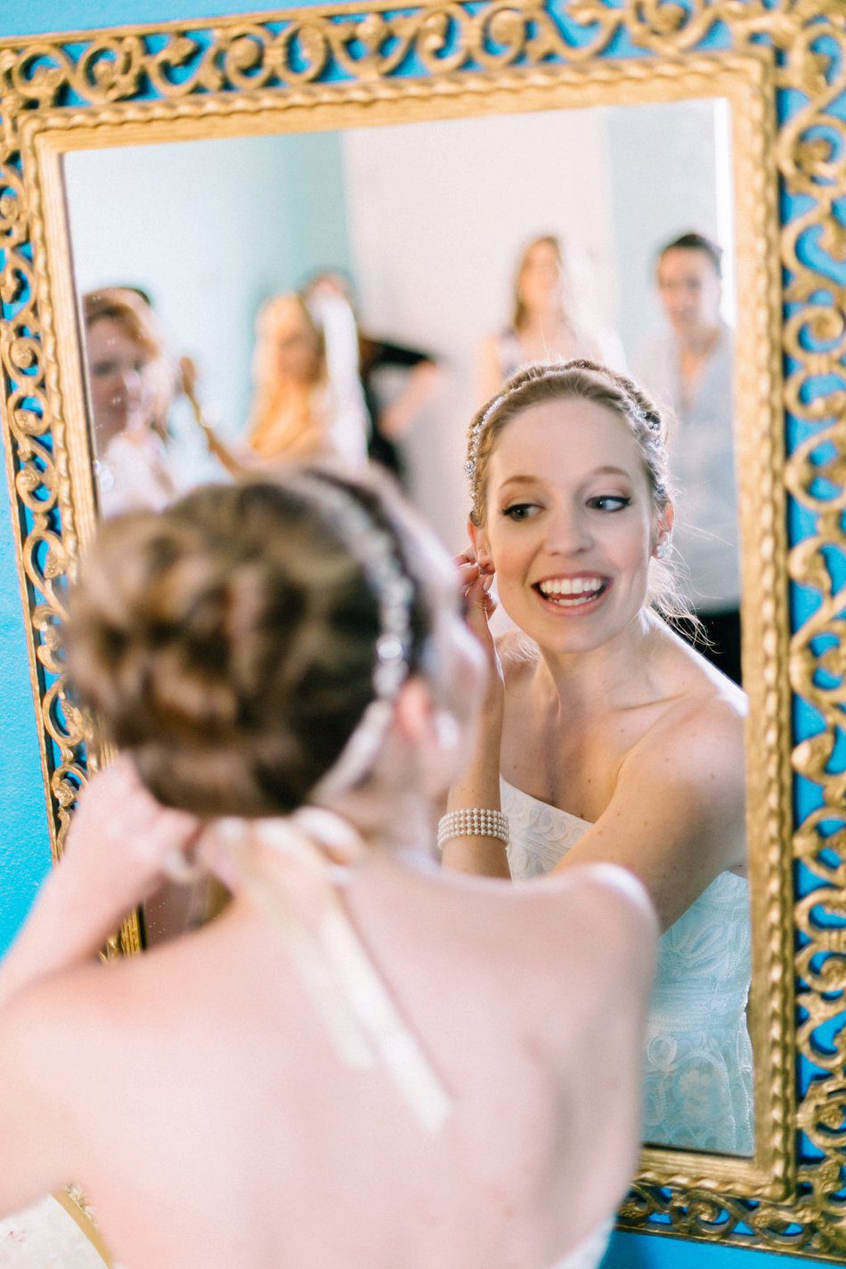 Must have wedding photo of bride putting her earrings on in mirror with bridesmaids in the background. Destination wedding at the Postcard Inn on the Beach by Catherine Ann Photography