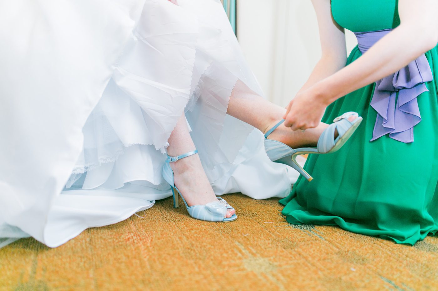 Bridesmaid putting on the brides blue wedding shoes