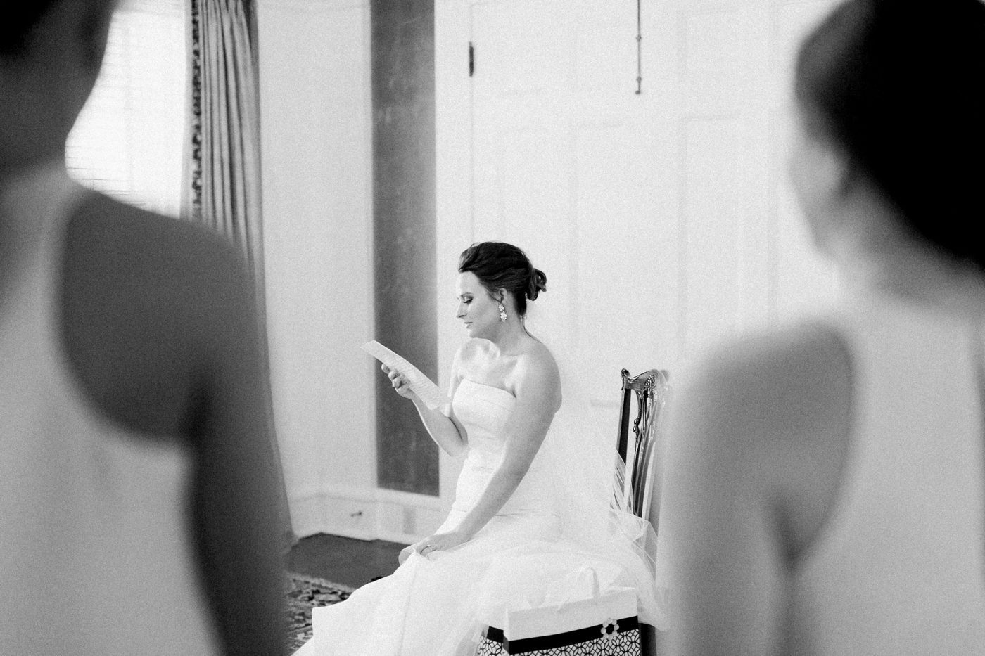 Creative wedding photography. Bride reading a letter from the groom with bridesmaids watching her. Photo by Charleston wedding photographer Catherine Ann Photography