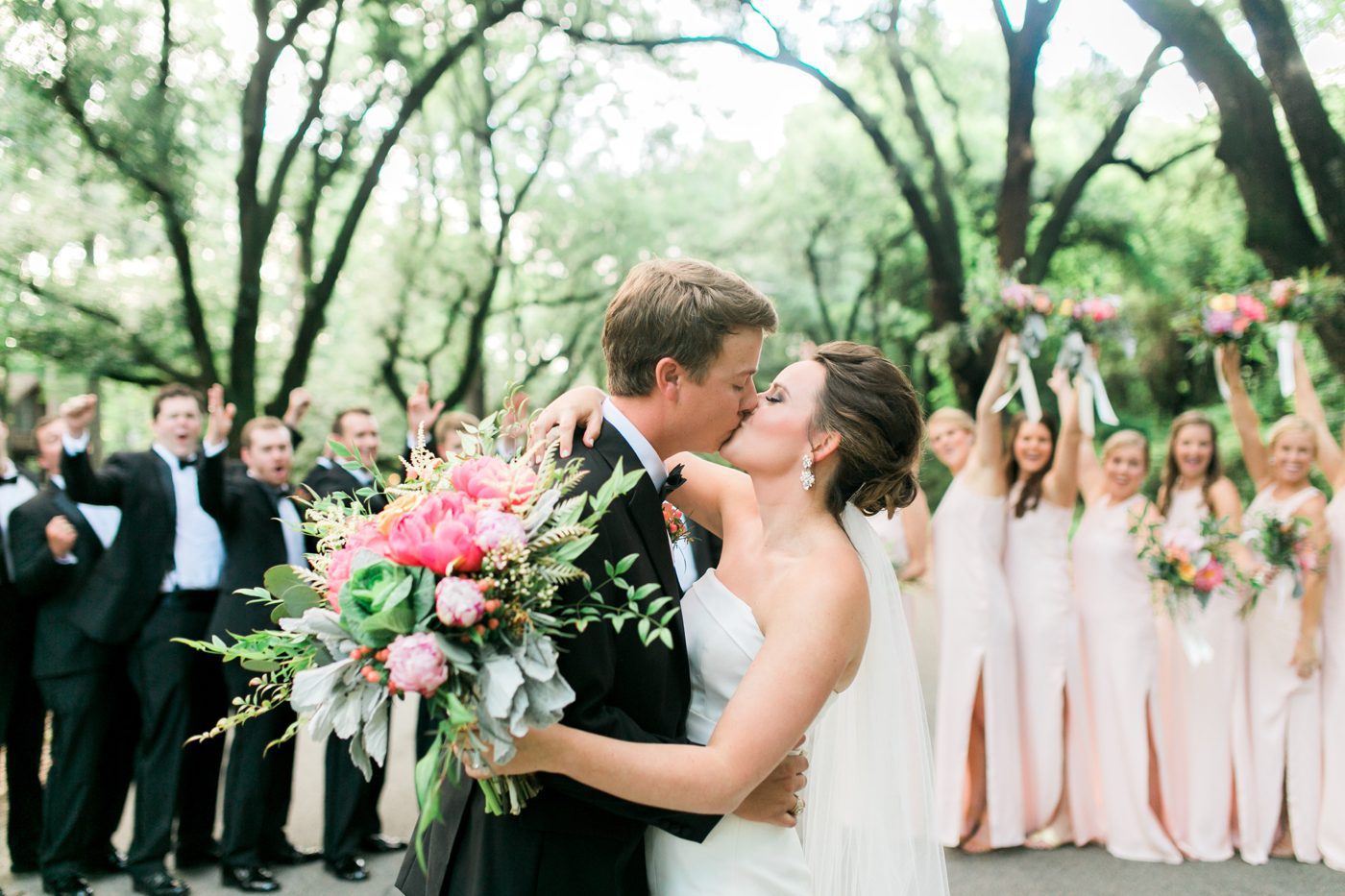 Best bridal photo idea bride and groom kissing with bridal party cheering in the background. Photo by Charleston wedding photographer Catherine Ann Photography