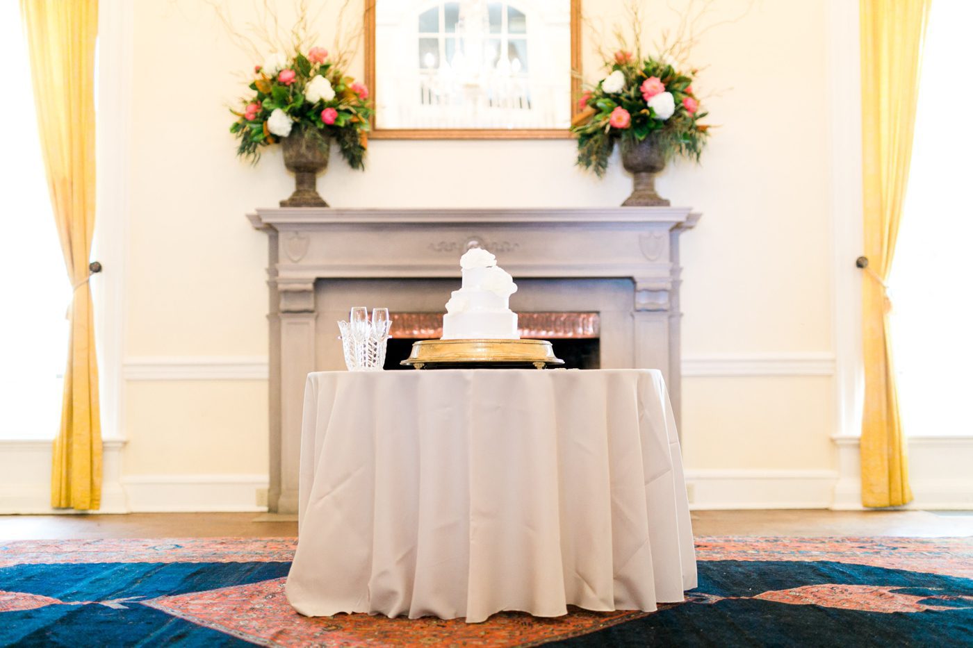 White wedding cake in front of old fireplace. Photo by Charleston wedding photographer Catherine Ann Photography