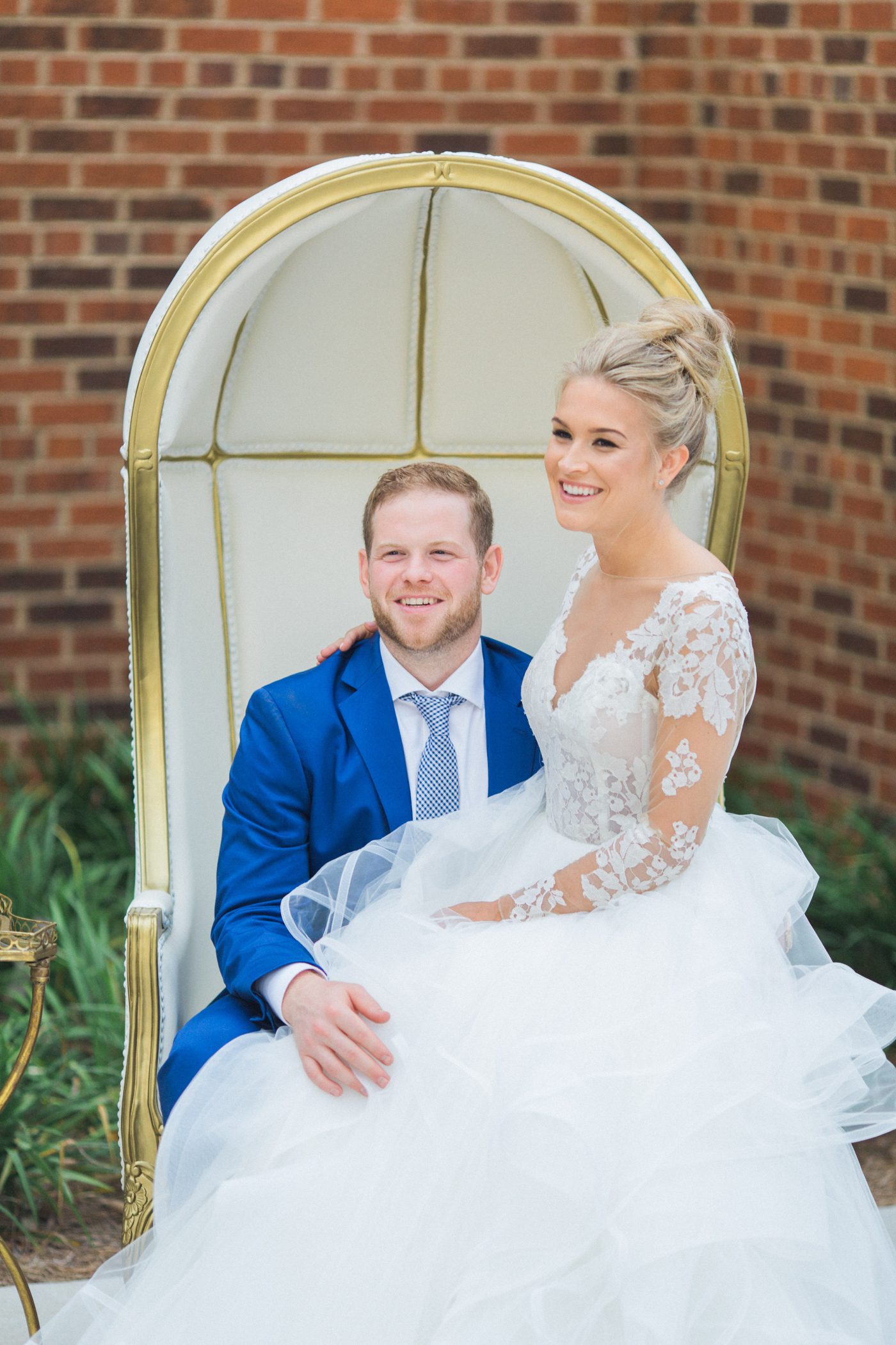 Portrait of bride sitting on grooms lap in giant white chair 