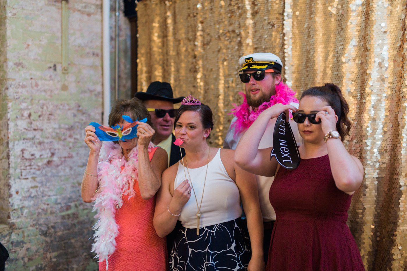 Guests using the photo booth with gold sequin back drop and props 