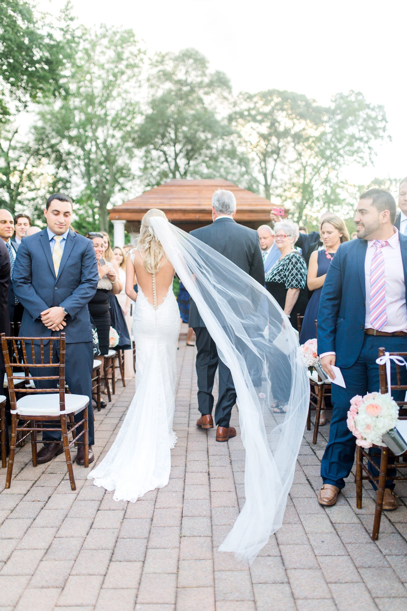 Brides veil flying in the wind as she walks down the aisle 