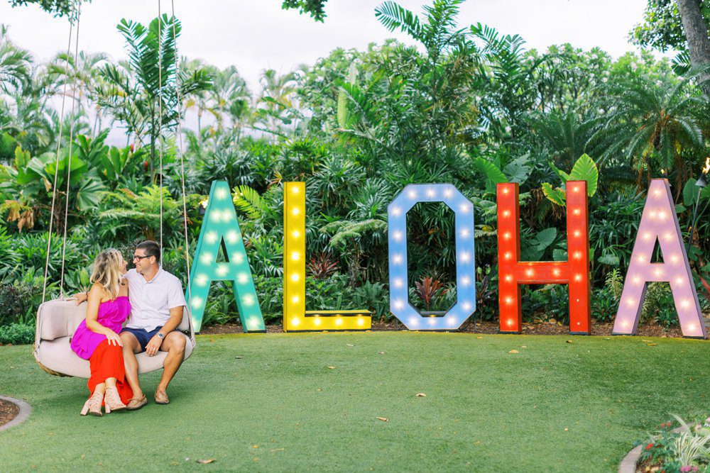 Maui HI engagement photo of couple wearing colorful outfits in front of a colorful Aloha sign at the Andaz Resort