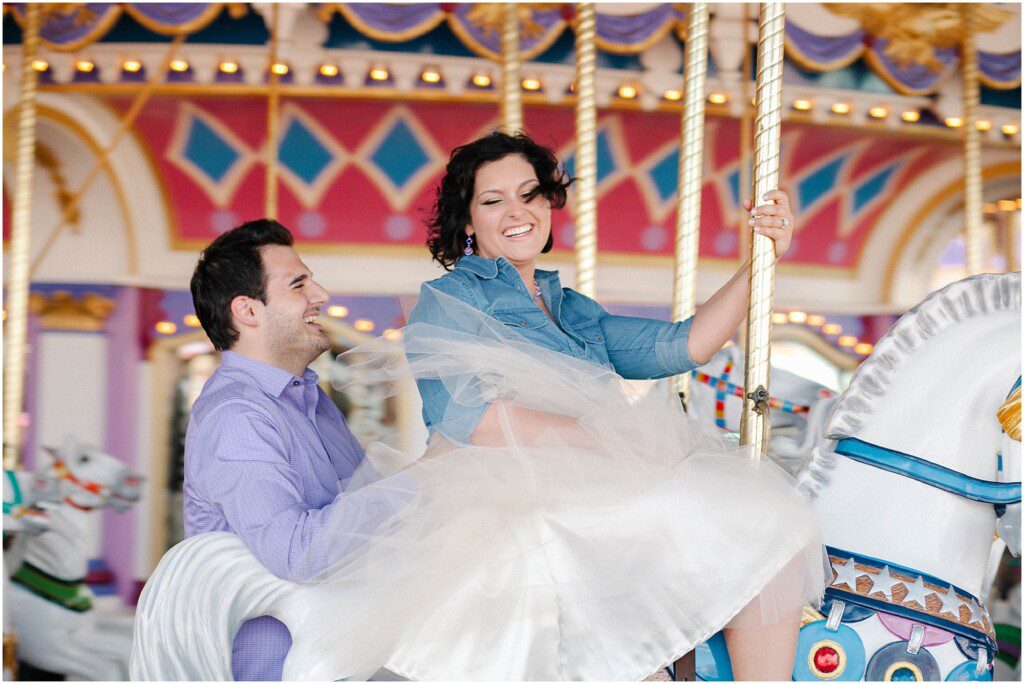 fun engagement photo of engaged couple riding the carousel at Disney World with the woman wearing a white tulle skir