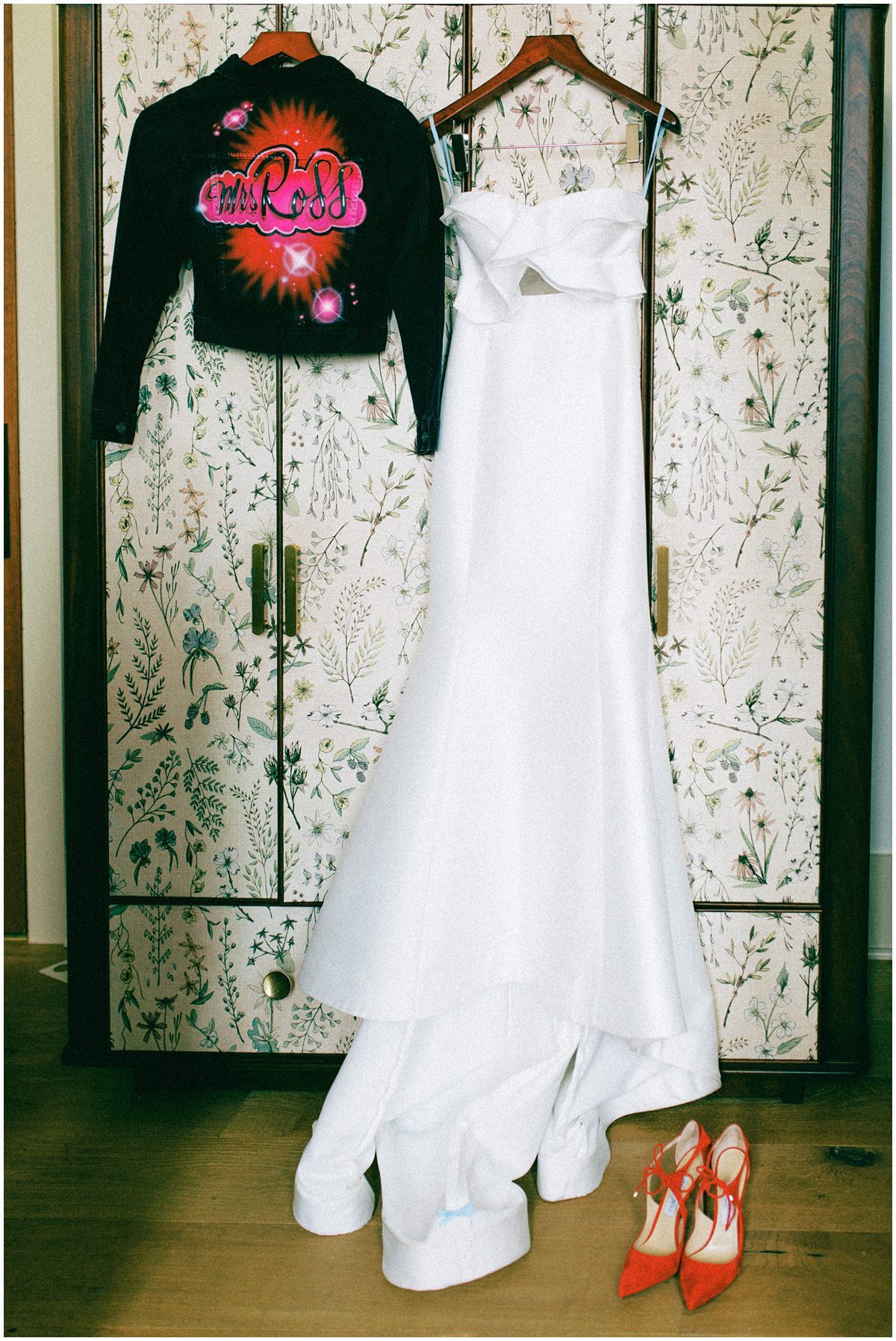 modern wedding gown hanging up with red jimmy choo shoes and fun spray paint jacket