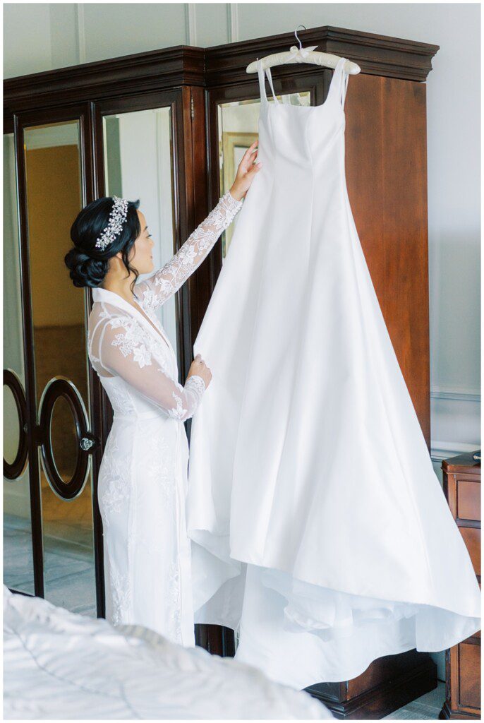 photo of bride looking at her wedding dress hanging up 