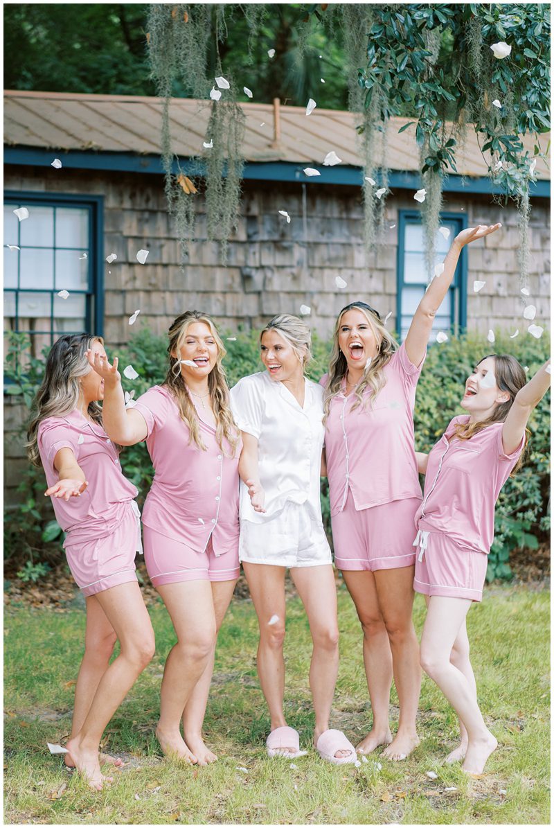 fun photo of bride and bridesmaids wearing pink silk pjs and throwing flower petals 