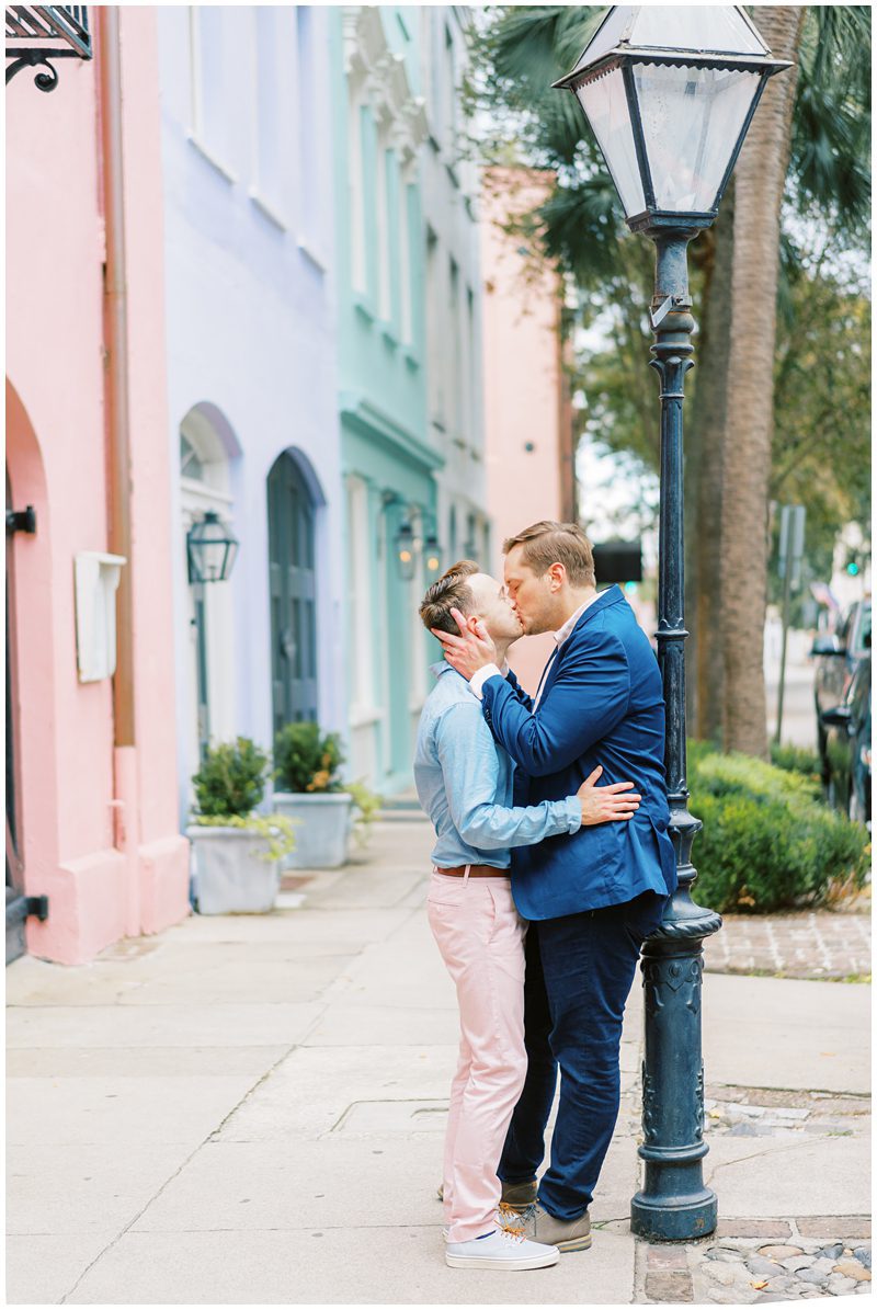 LGBTQ engagement photo of two men kissing in colorful suits at Rainbow Row in Charleston SC