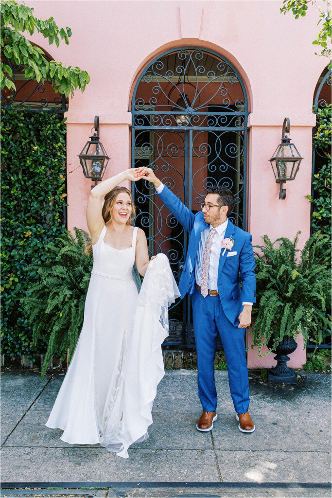 groom twirling the bride in front of a pink house in Charleston 