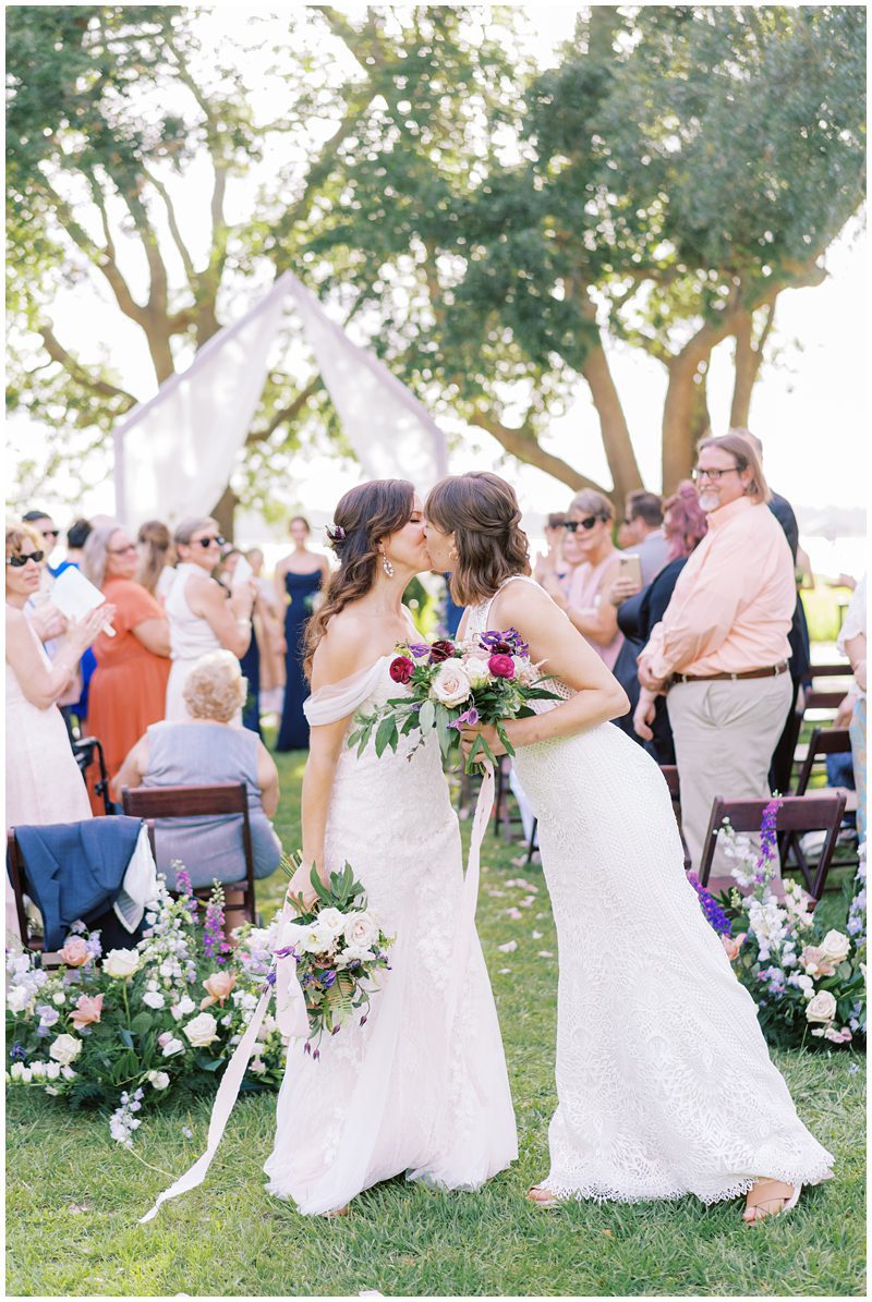 Candid wedding photo of two brides kissing at wedding ceremony at Lowndes Grove