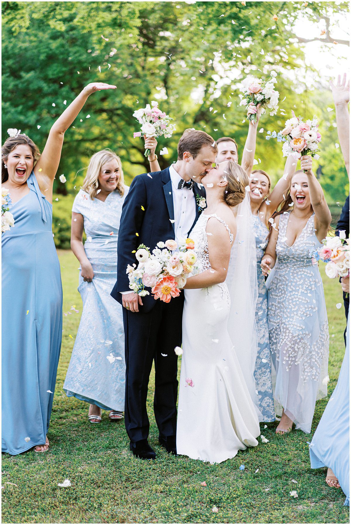 fun wedding party photo of bridesmaids dressed in blue throw flower petals at the bride and groom