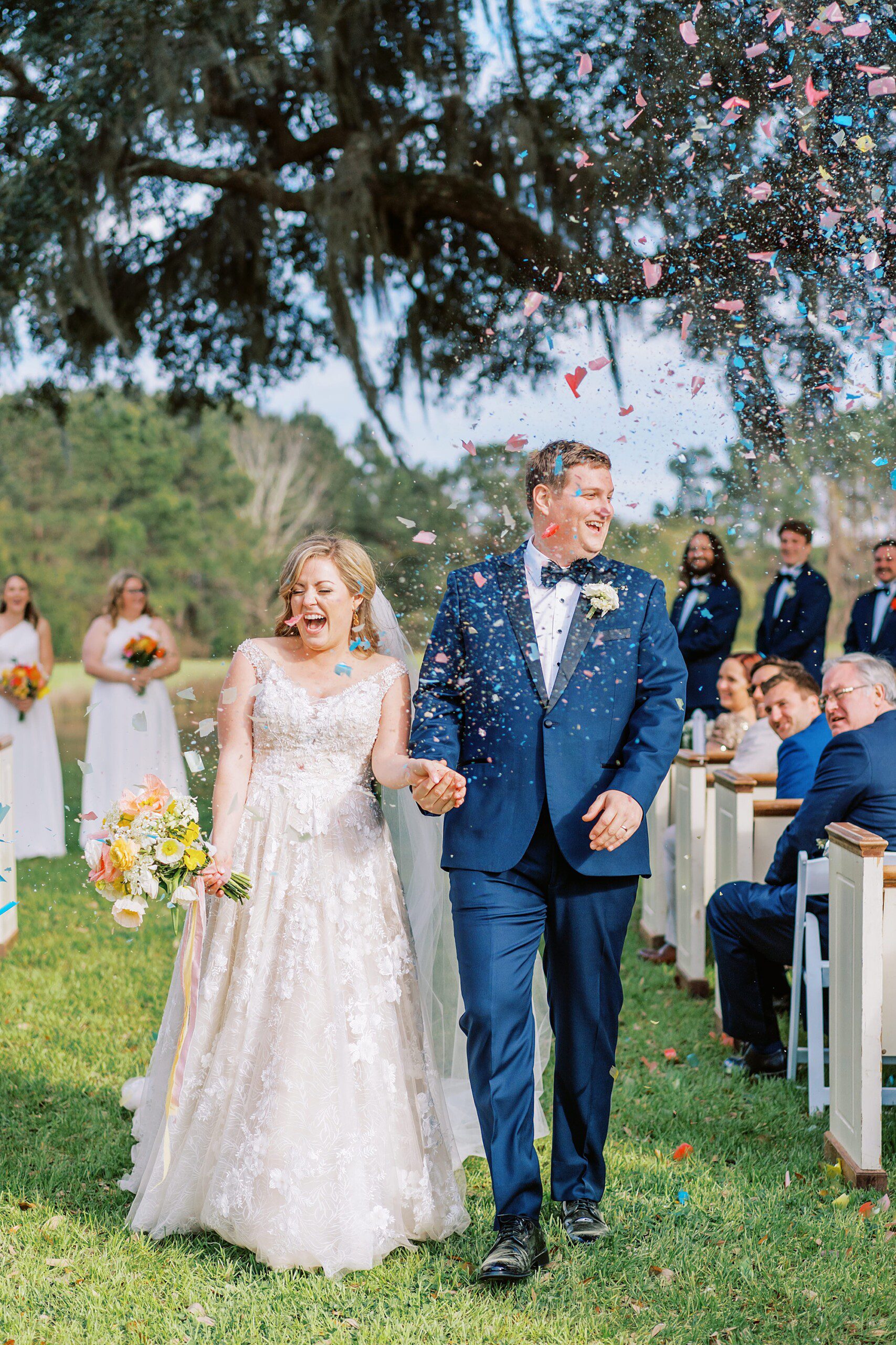 Bride and groom laughing as they walk down the aisle after getting married in Charleston and guests throw rainbow confetti at them