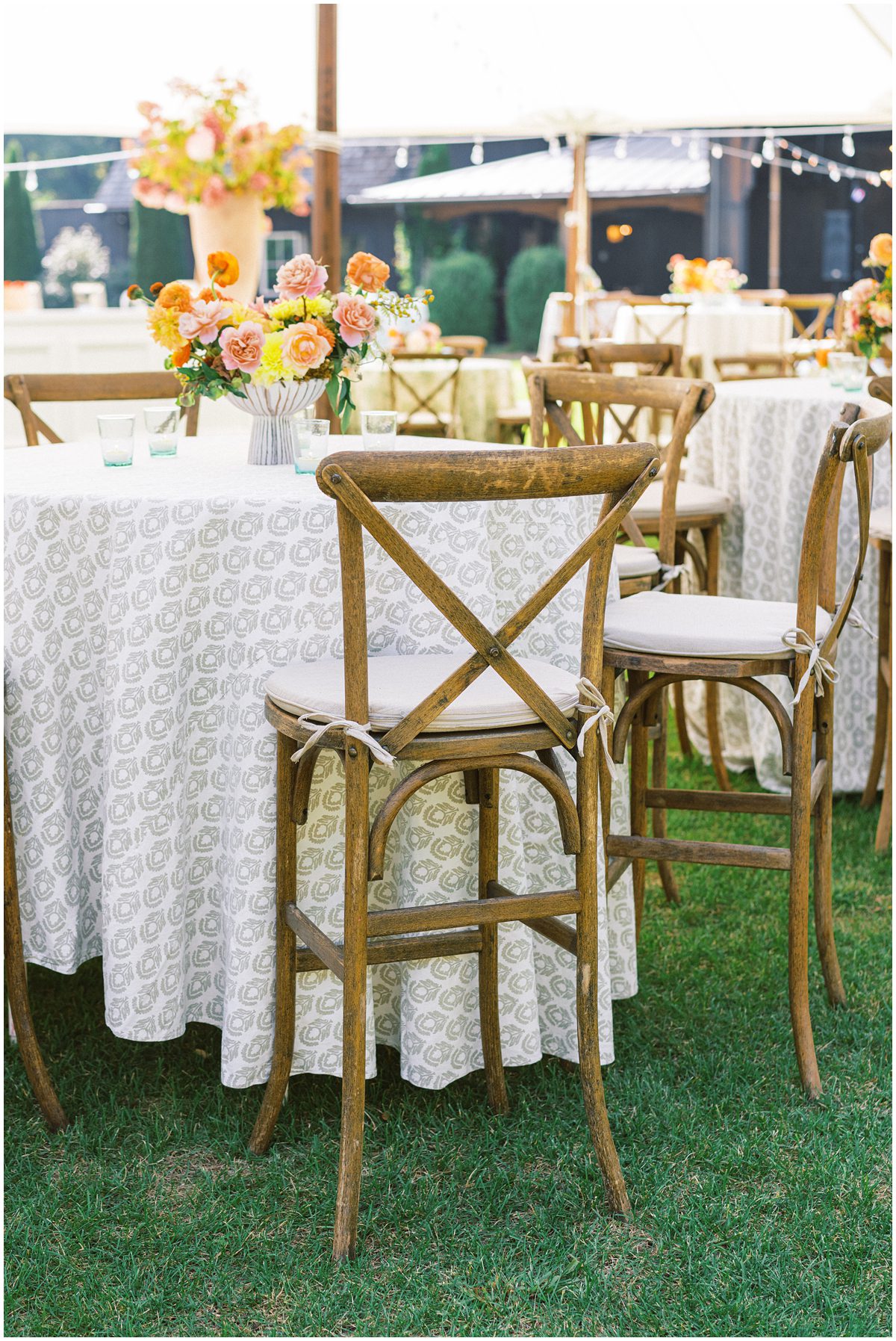 Hightop cocktail tables at a wedding with lux pattern linens, yellow, pink and orange flowers and tall wooden cross back chairs