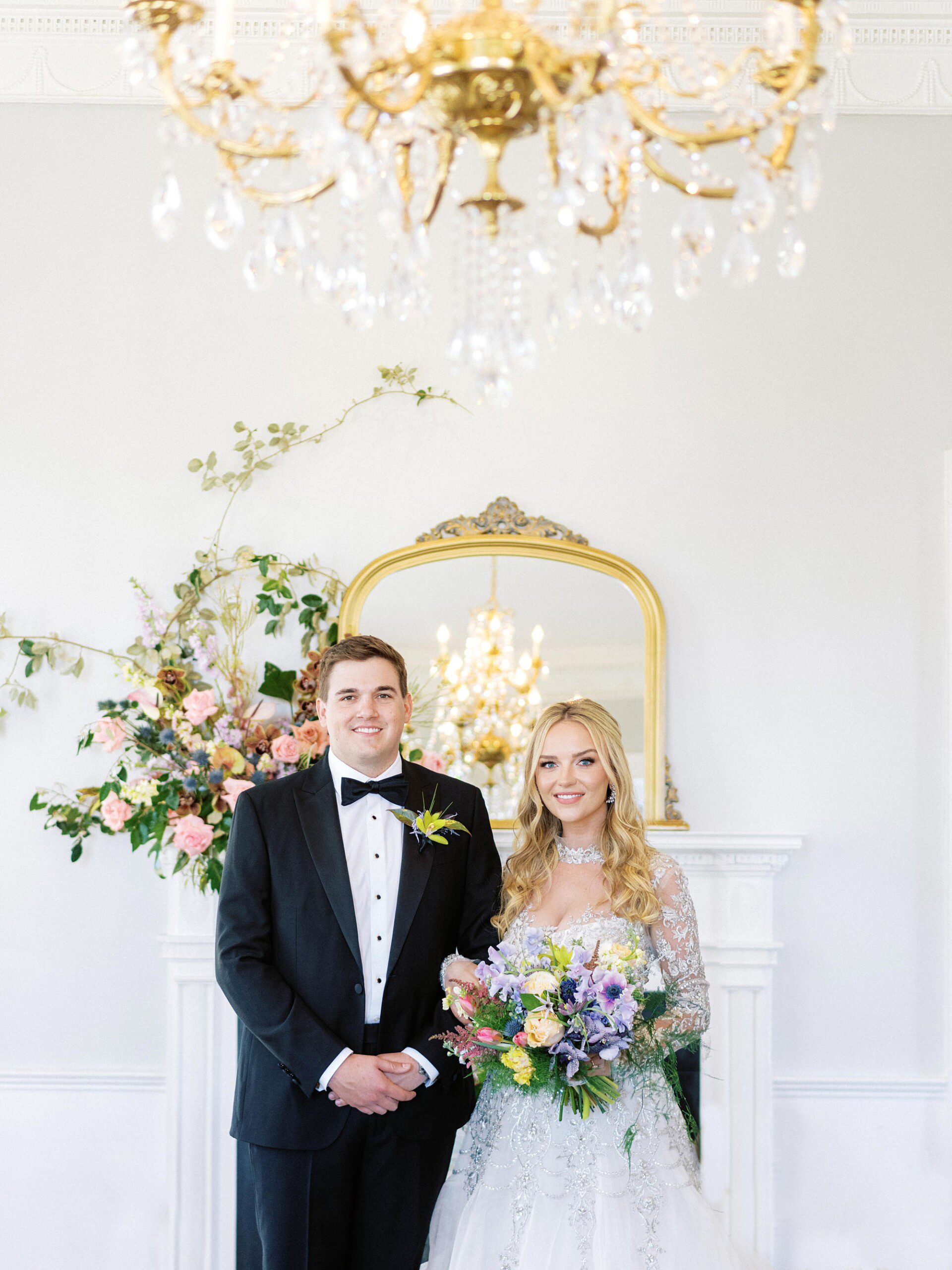 Bride and groom standing in front of a floral installation at their Charleston SC wedding venue, the Gadsden House