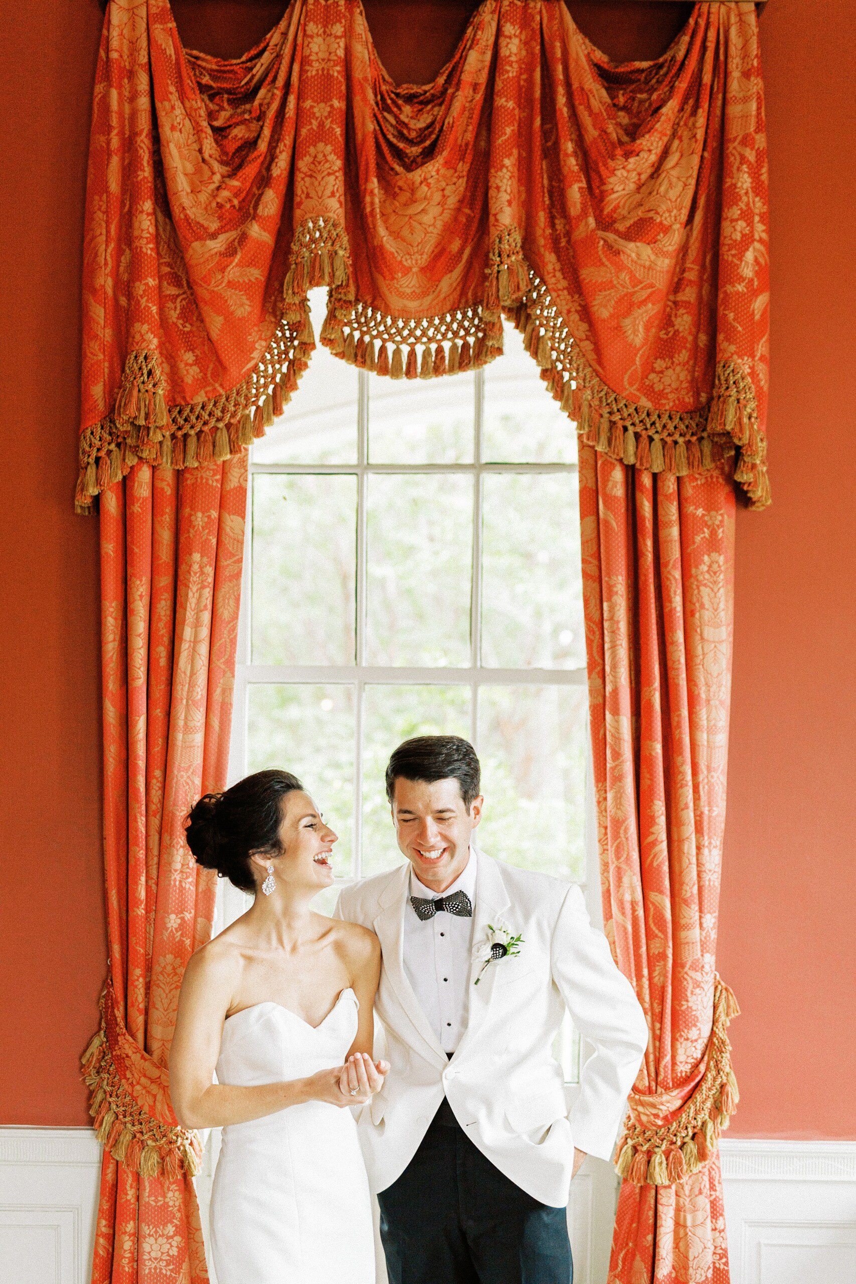A bride and groom laughing in the red room at the William Aiken House
