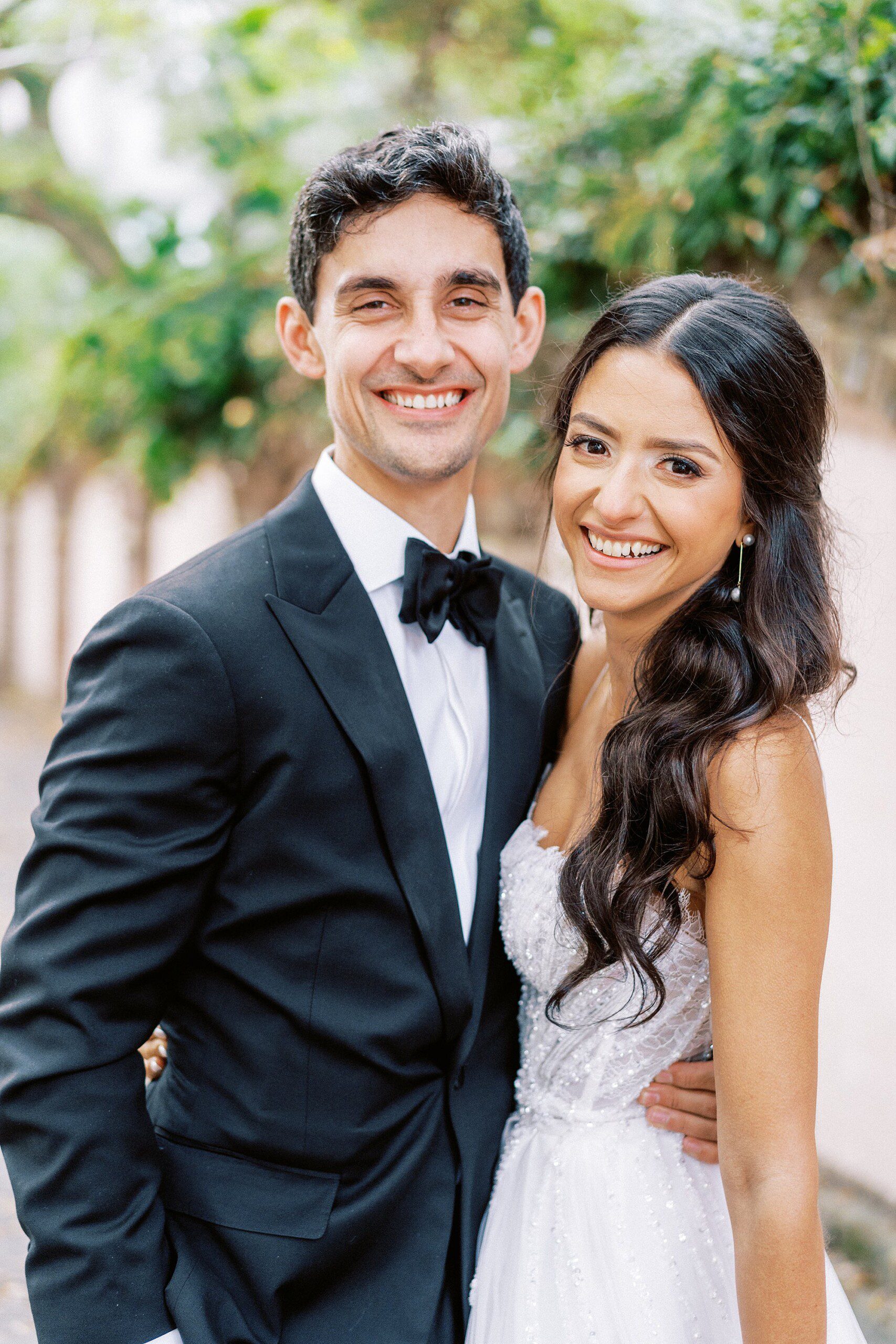 classic portrait of a groom wearing a fitted black tux and a bride wearing a sparkly wedding dress smiling at the camera at Cannon Green