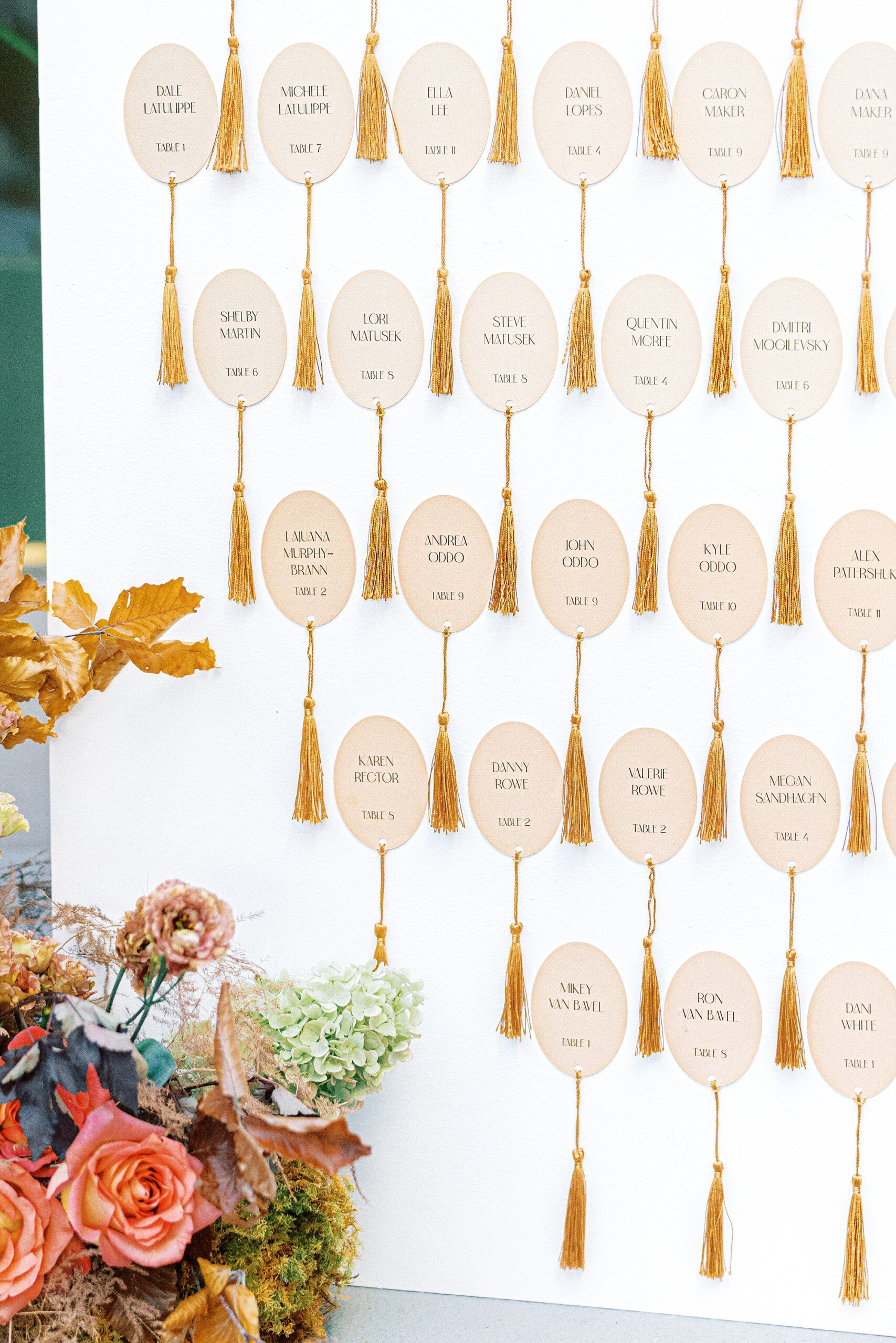 a luxurious escort card display with rounded paper and golden tassels surrounded by vibrant florals at Hotel Emeline wedding
