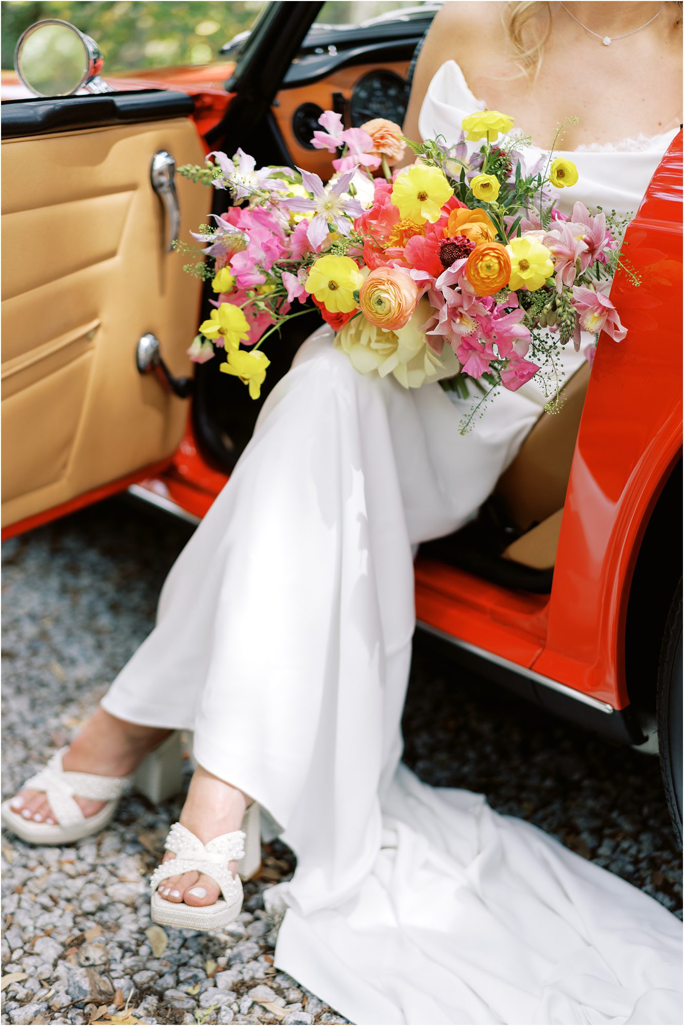 A colorful bridal bouquet and white wedding gown inside a vintage red car, captured by a Florida wedding photographer