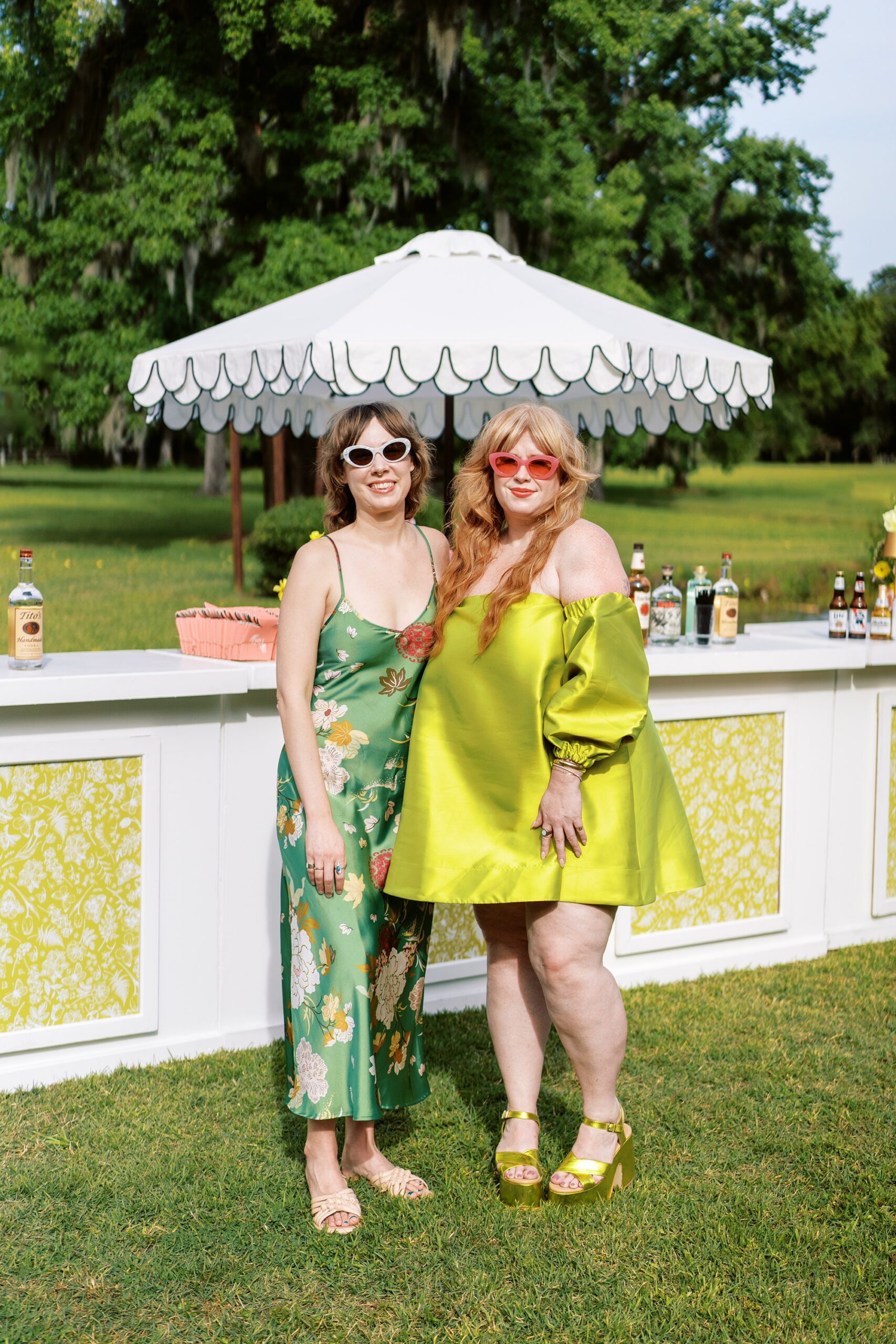 Two fashion-forward wedding guests in stylish, colorful dresses posing by an outdoor cocktail bar at a luxury wedding in Sarasota Florida