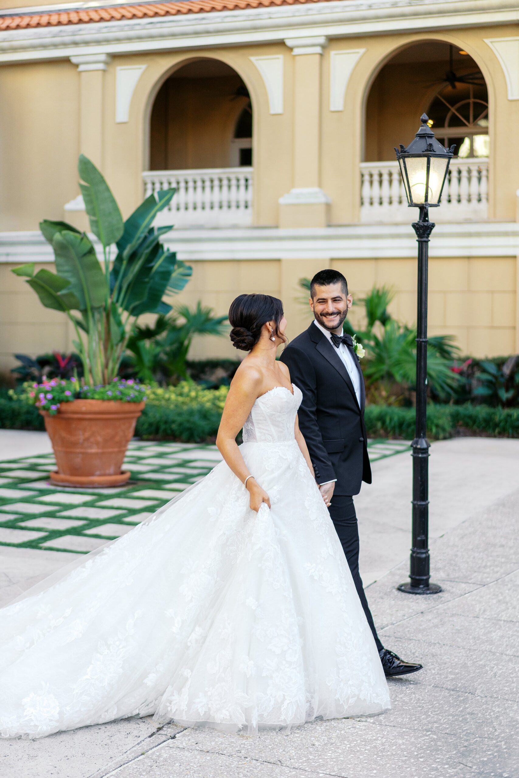 An fashionable bride in a ballgown and a groom in a classic black tuxedo walking in the courtyard at a Ritz Carlton Sarasota wedding