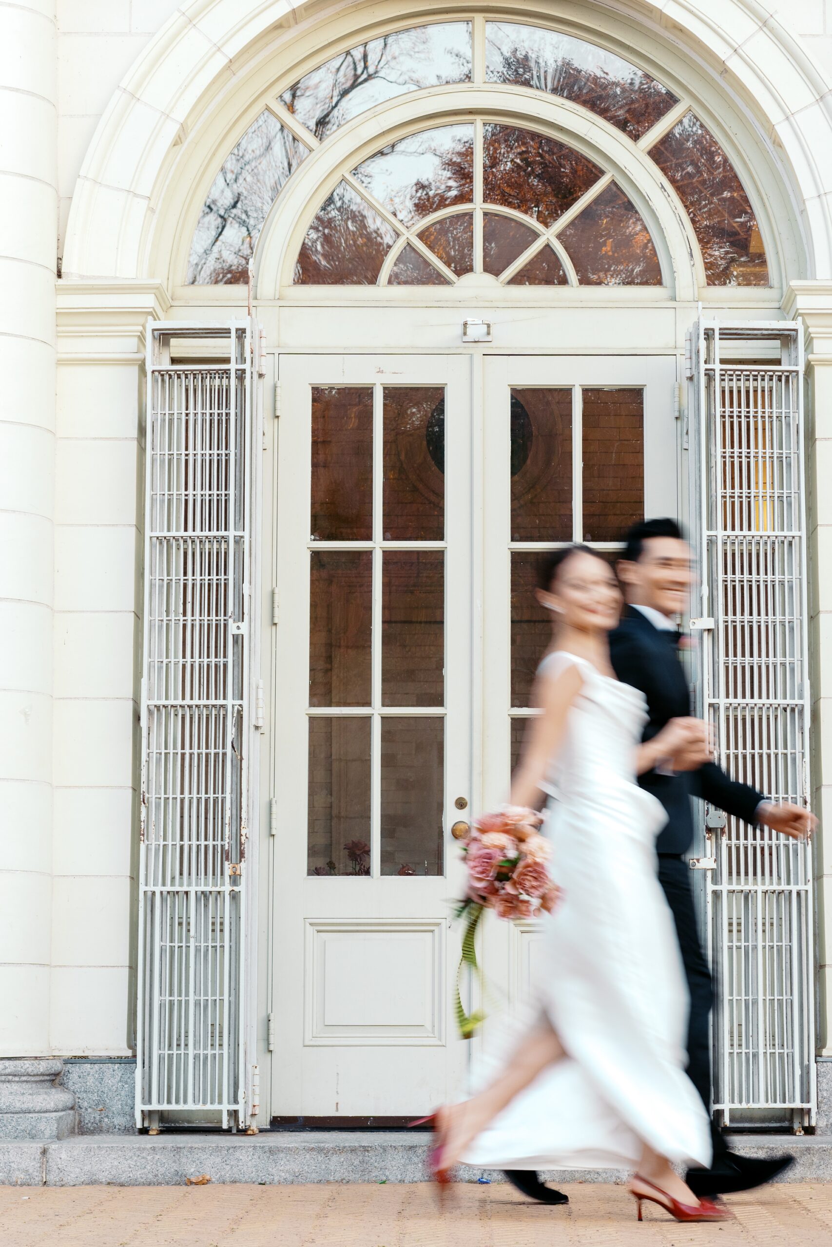 Fashionable bride and groom wearing Prada running hand in hand outside Purslane at the Prospect Park Boathouse in Brooklyn, NY by New York wedding photographer Catherine Ann Photography