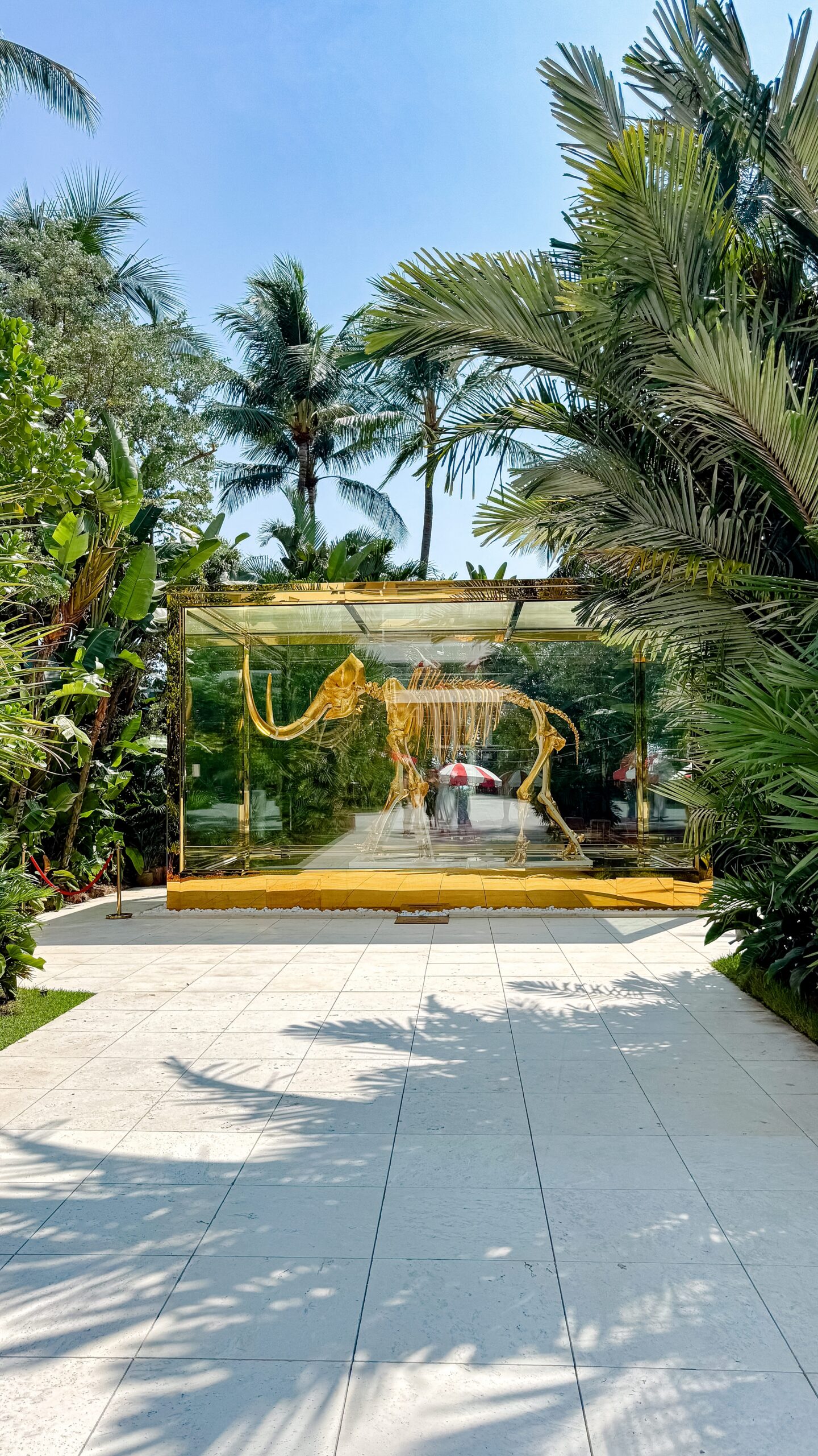 Gold mammoth skeleton in a glass display surrounded by lush tropical palms in the Mammoth Garden at Faena Miami Beach.